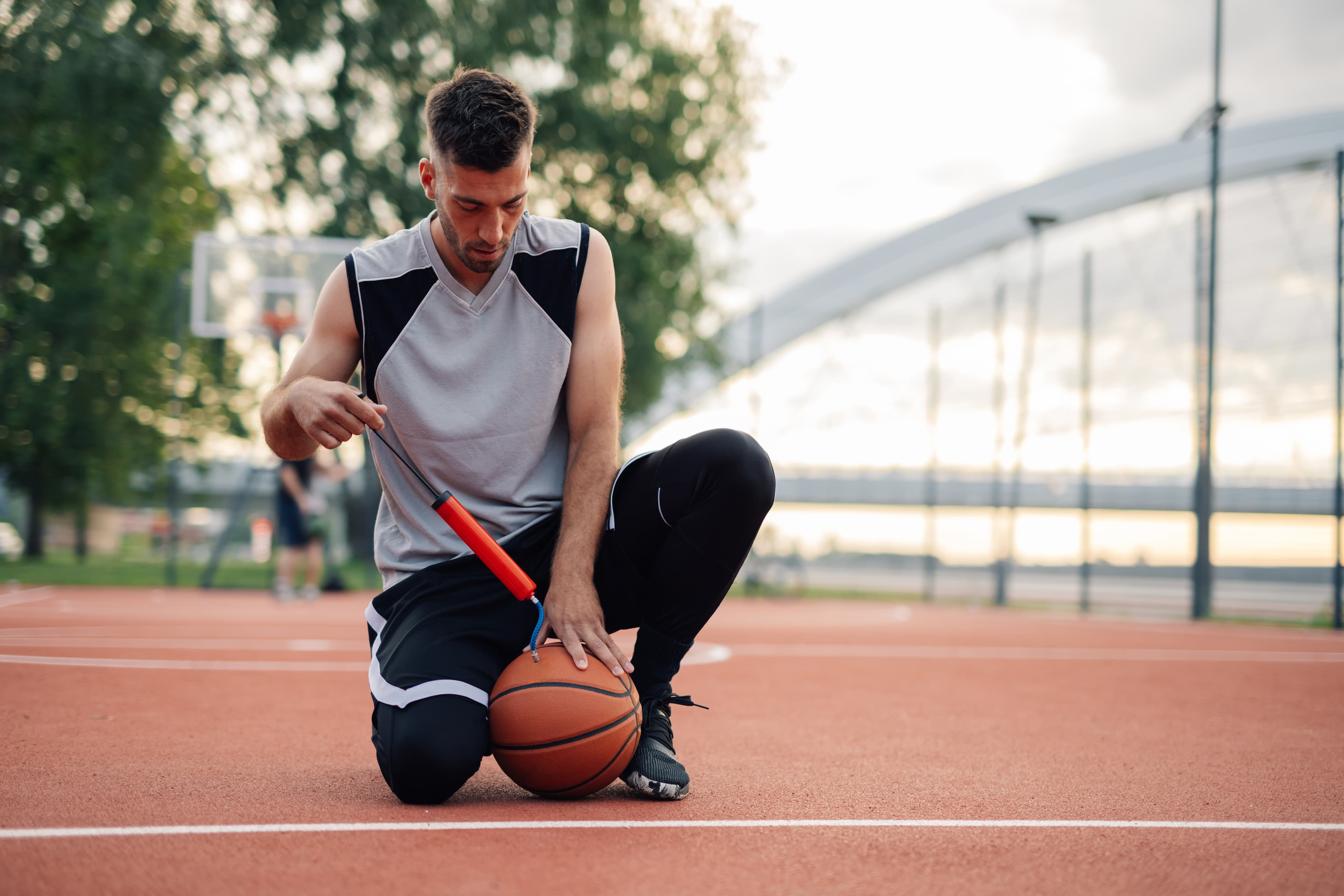 Athlete kneeling on a court to inflate a basketball
